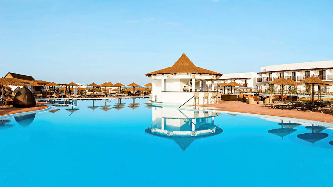 Et stort basseng med parasoller og sitteplasser ved et hotellområde. (AI-generert tekst)