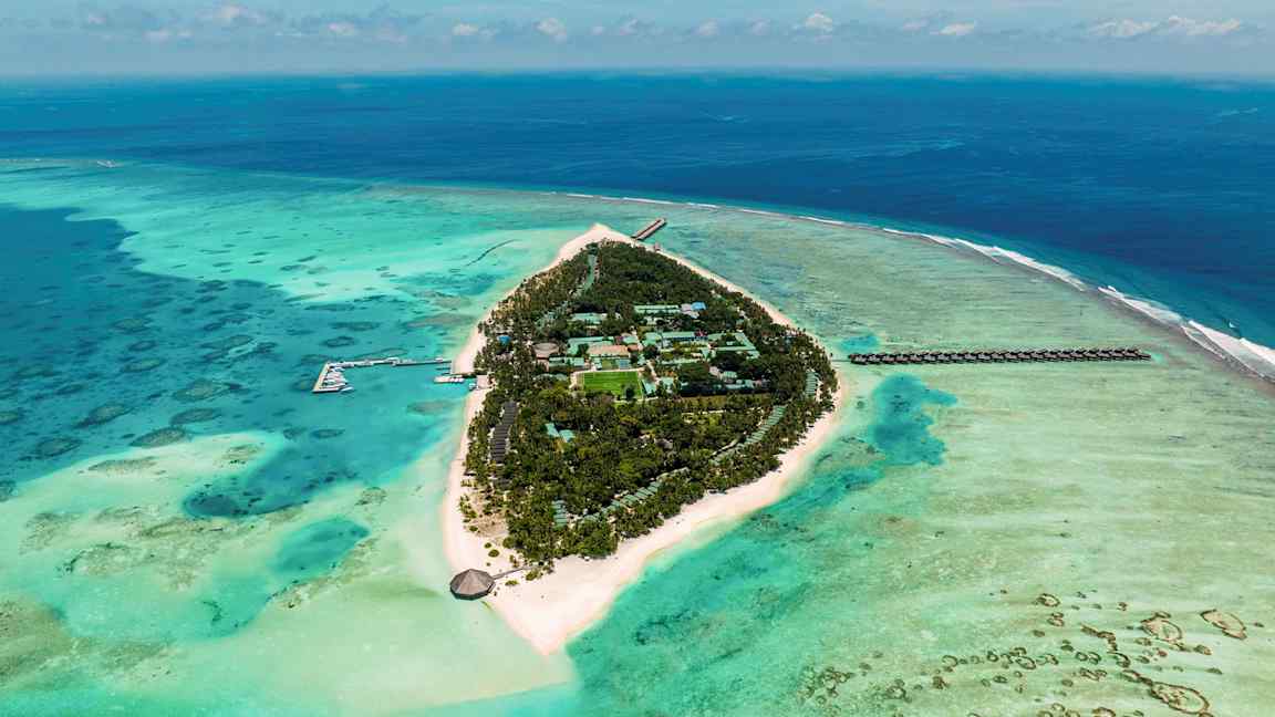 Flyfoto av en tropisk ø omgitt av turkis hav med hvite sandstrender og grønn vegetasjon. (AI-generert tekst)