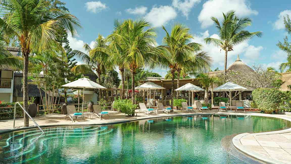 Et eksotisk basseng omgitt av palmetrær og solsenger under parasoller. (AI-generert tekst)