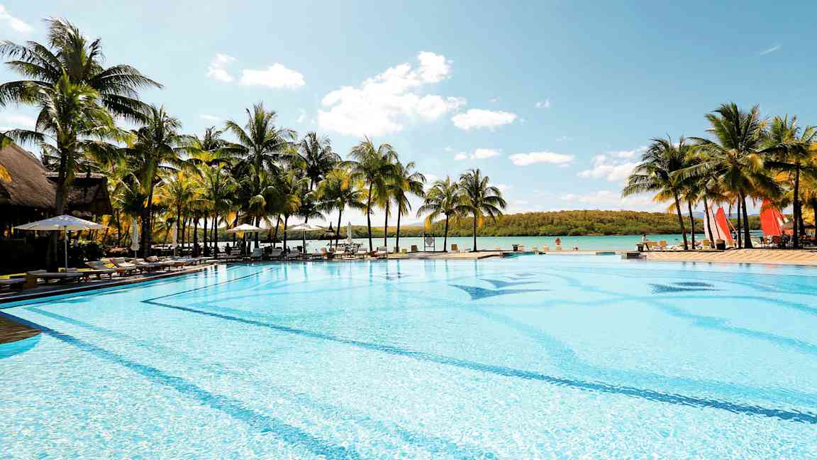 Stor basseng ved sjøen omgitt av palmer. (AI-generert tekst)