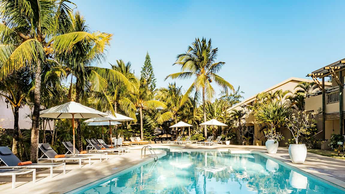 Bassengområde med solsenger og parasoller, omgitt av palmer. (AI-generert tekst)
