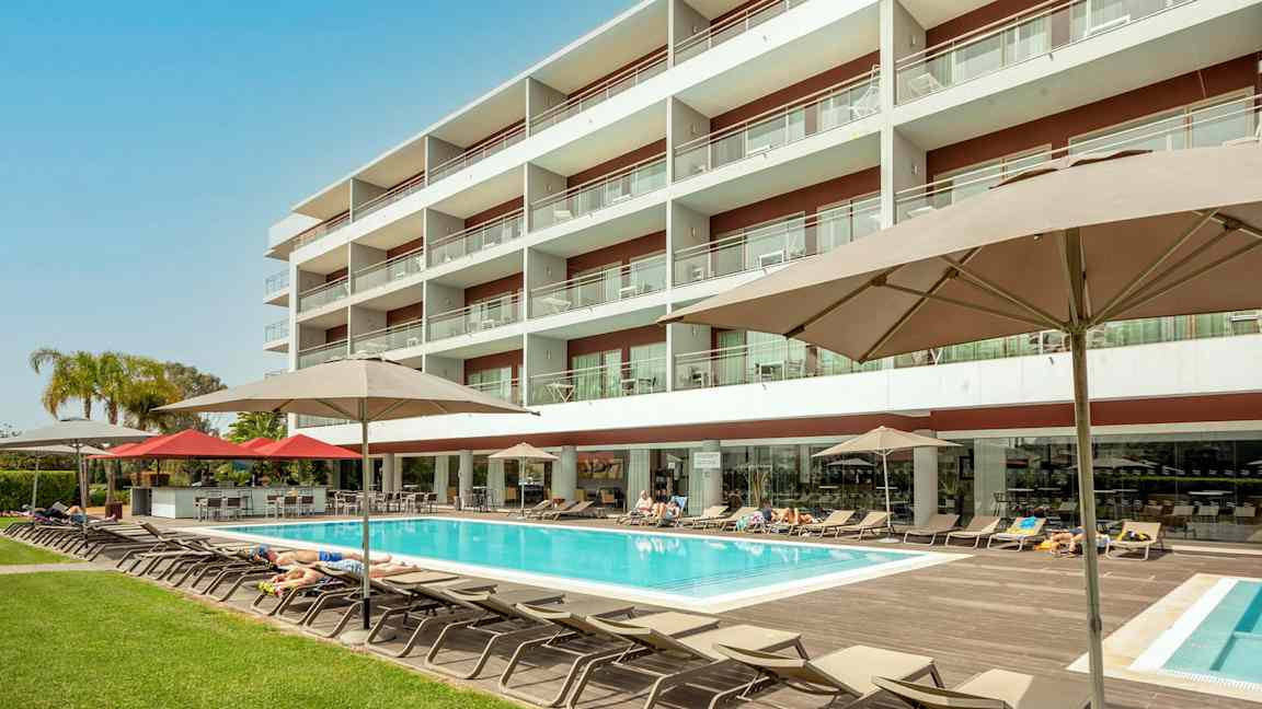 Hotellbygning med basseng og solsenger. (AI-generert tekst)