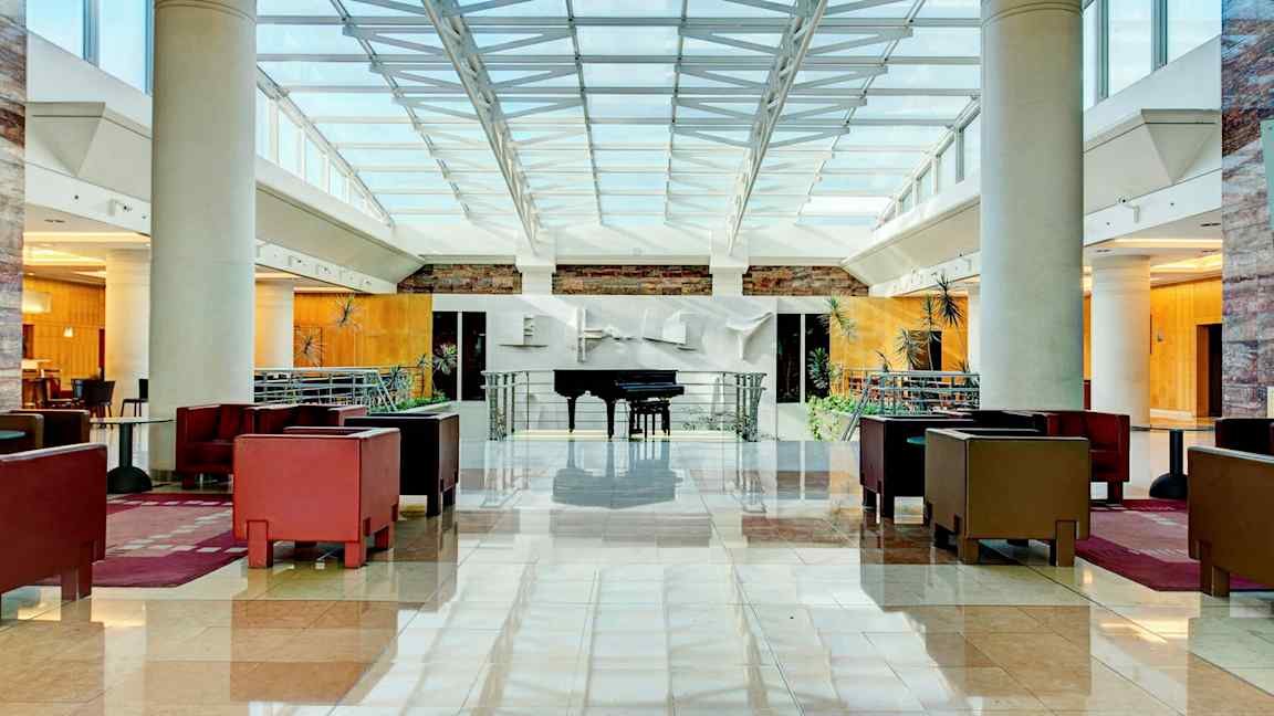 Lys og romslig hotellobby med sittegrupper og et piano. (AI-generert tekst)