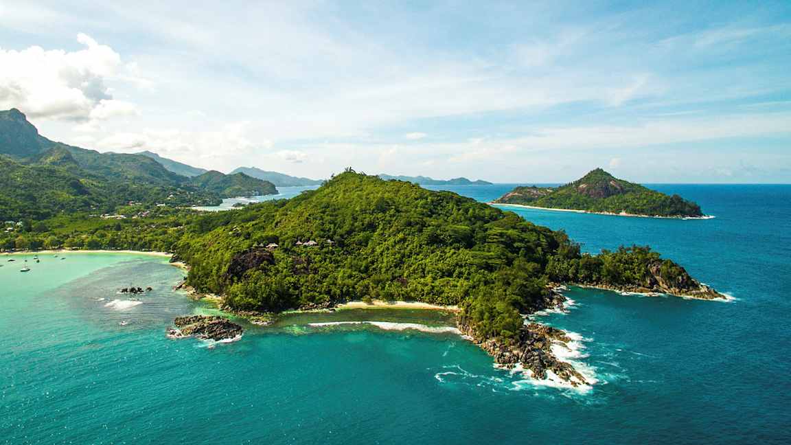 Luftfoto av en frodig ø omgitt av klarblått hav og mindre øyer i bakgrunnen. (AI-generert tekst)