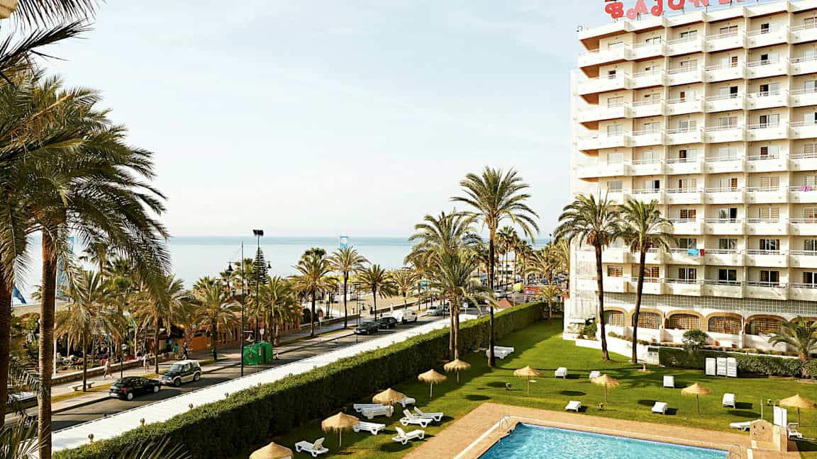 Bilde av et hotell med basseng, palmer og utsikt over havet. (AI-generert tekst)