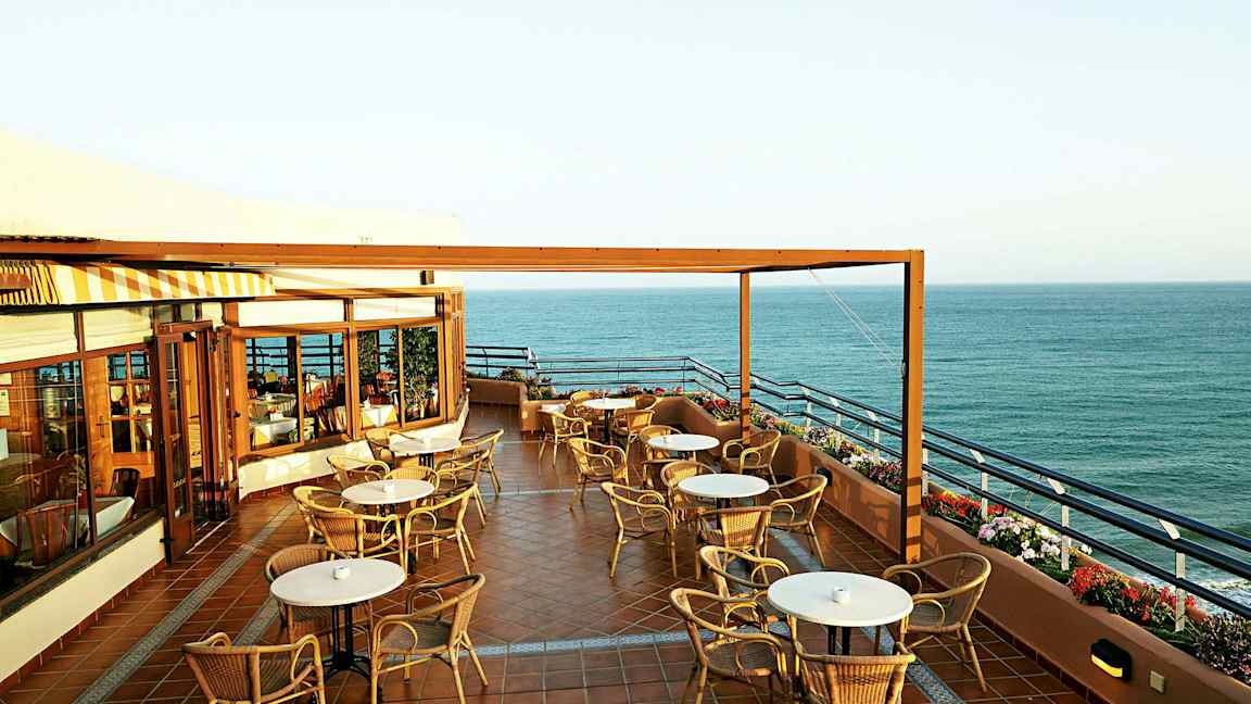 En terrasse med bord og stoler og utsikt over havet. (AI-generert tekst)