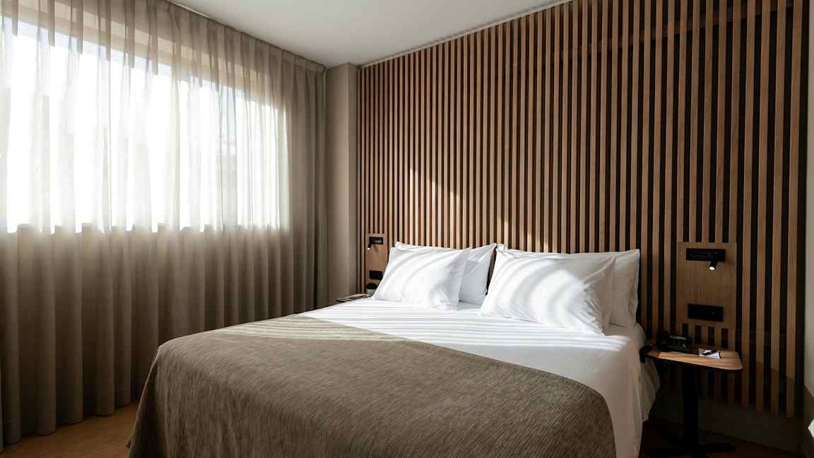 En seng i et moderne soverom med trepanel og lysinnslipp fra et vindu. (AI-generert tekst)