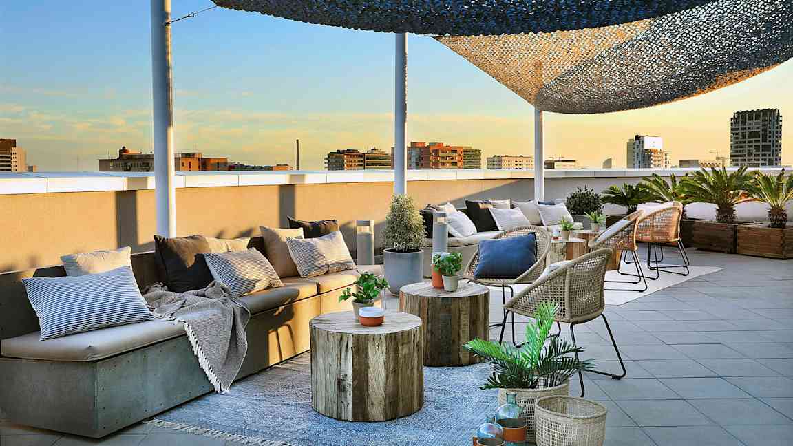 En takterrasse med sittemøbler, bord og kurver dekorert med planter og puter er avbildet. (AI-generert tekst)