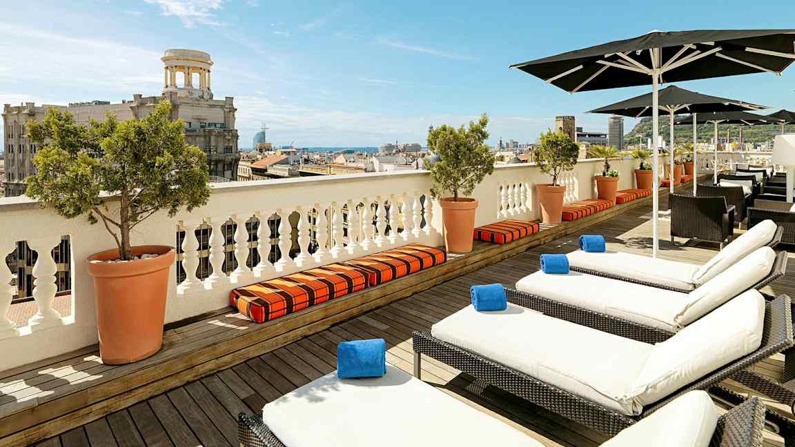 Utsikt over en terrasse med solsenger og parasoller, med en by og havet i bakgrunnen. (AI-generert tekst)