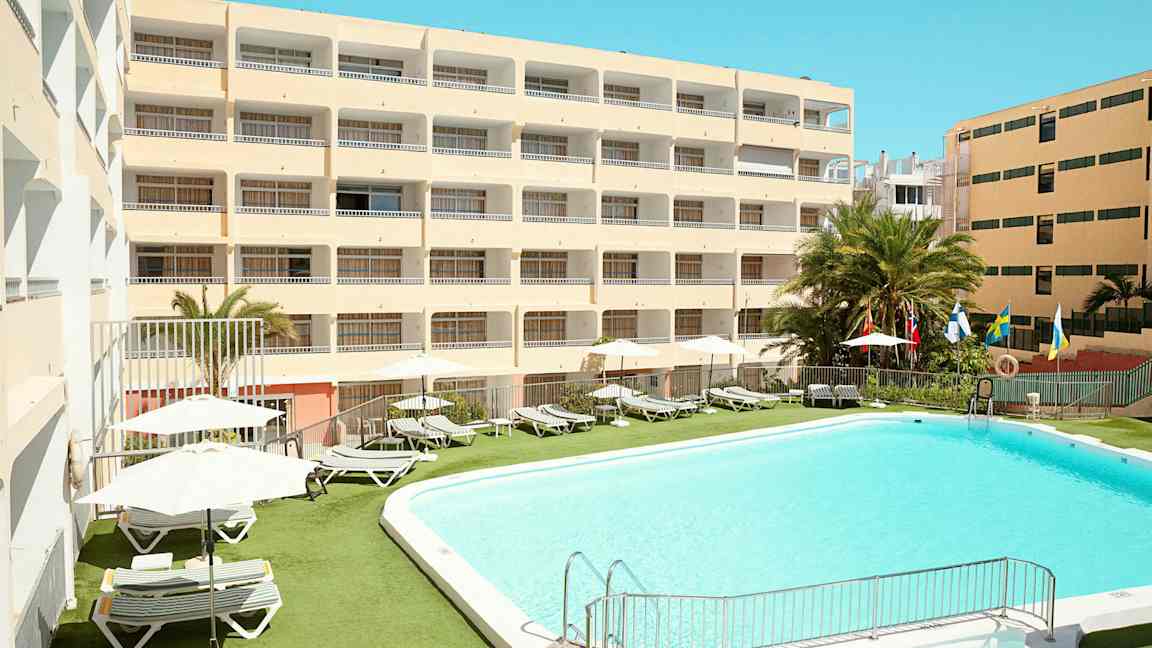 Hotellbygning med basseng og solsenger utendørs. (AI-generert tekst)