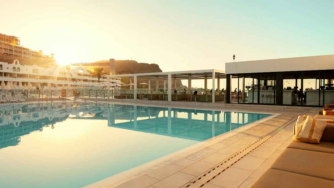 Utendørs svømmebasseng ved et hotell med solsenger og en bygning i bakgrunnen. (AI-generert tekst)