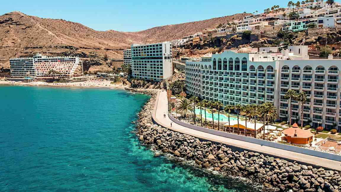 Hotell ved en kyst med klipper, basseng og palmer. (AI-generert tekst)