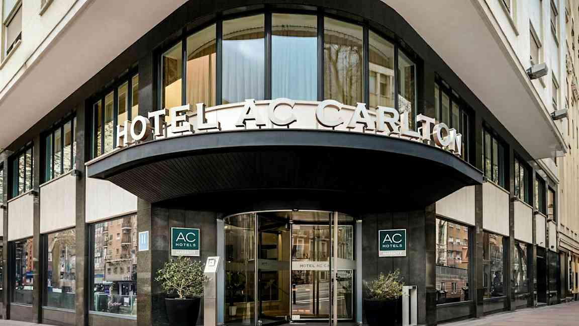 En hotellfasade med skilteteksten "HOTEL AC CARLTON" synlig over inngangen. (AI-generert tekst)