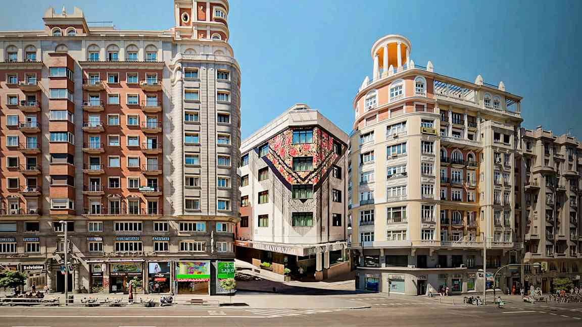 Tre bygninger ligger langs en gate, hvor midtbygningen har fargerike kunstverk på fasaden. (AI-generert tekst)