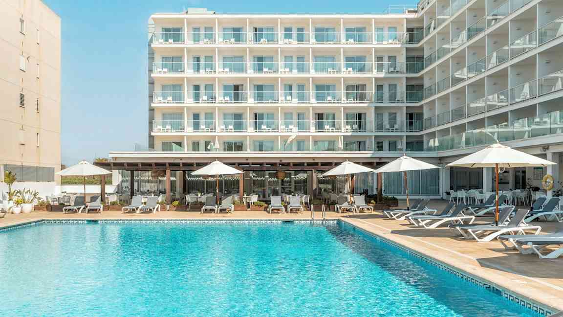 En bygning med flere balkonger, foran et basseng med solsenger og parasoller. (AI-generert tekst)