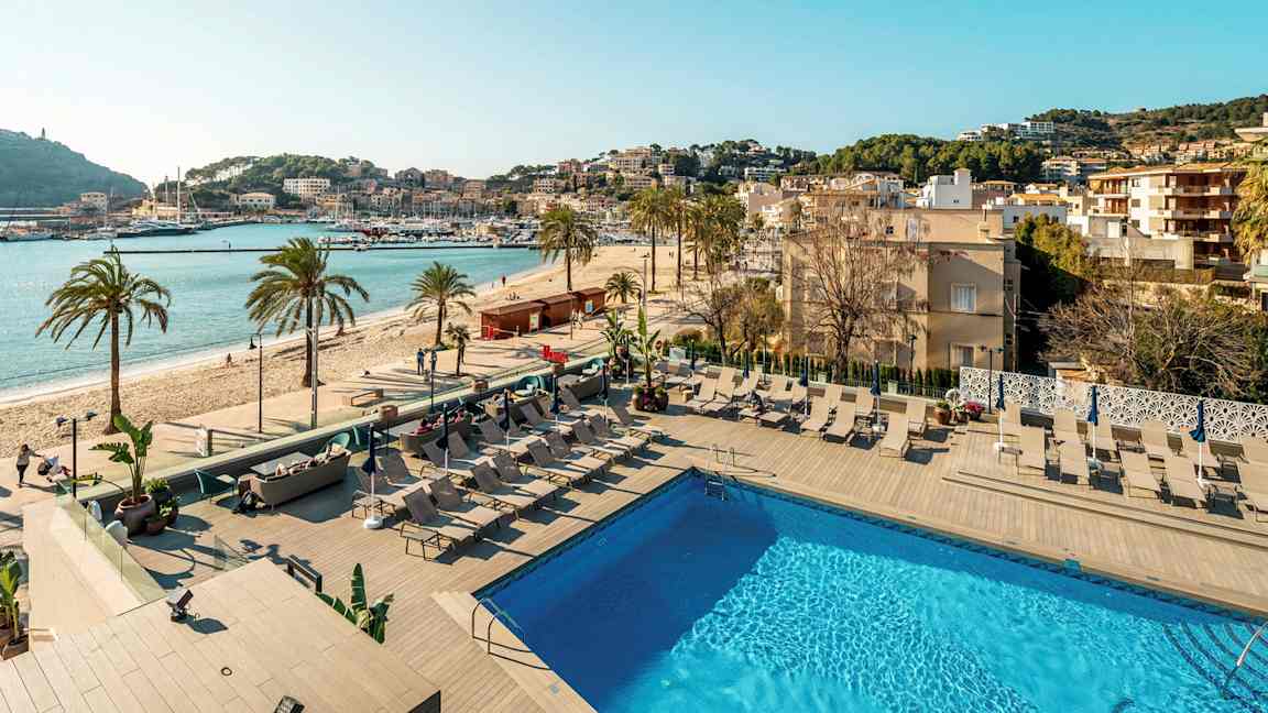 Utendørs basseng med solsenger og utsikt mot stranden og en havn. (AI-generert tekst)