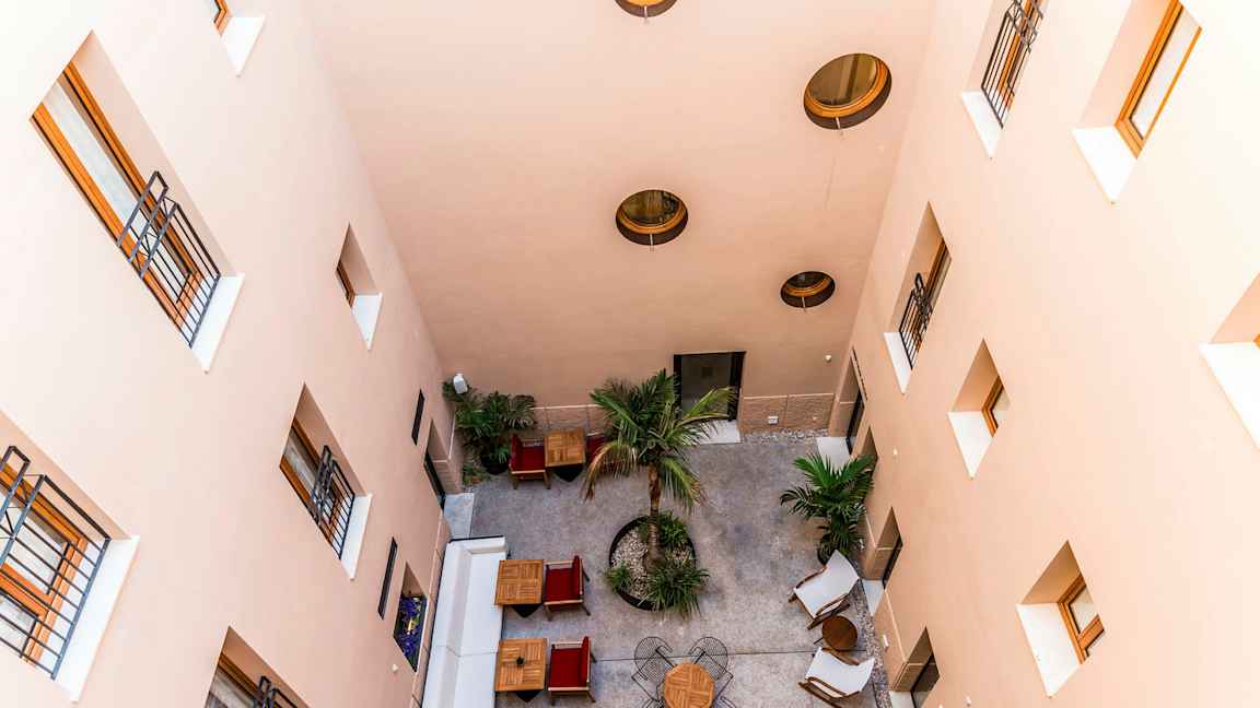 En indre gårdsplass sett ovenfra med bord, stoler og trær. (AI-generert tekst)