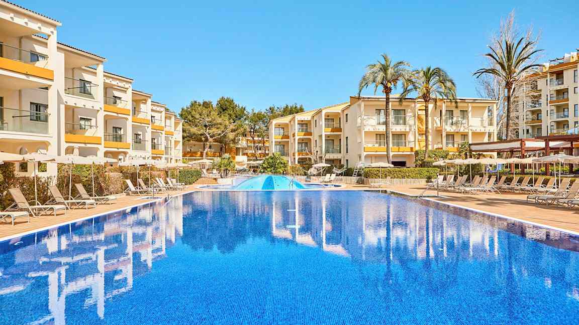 Bilde av et utendørsbasseng med bygninger og solsenger i bakgrunnen. (AI-generert tekst)