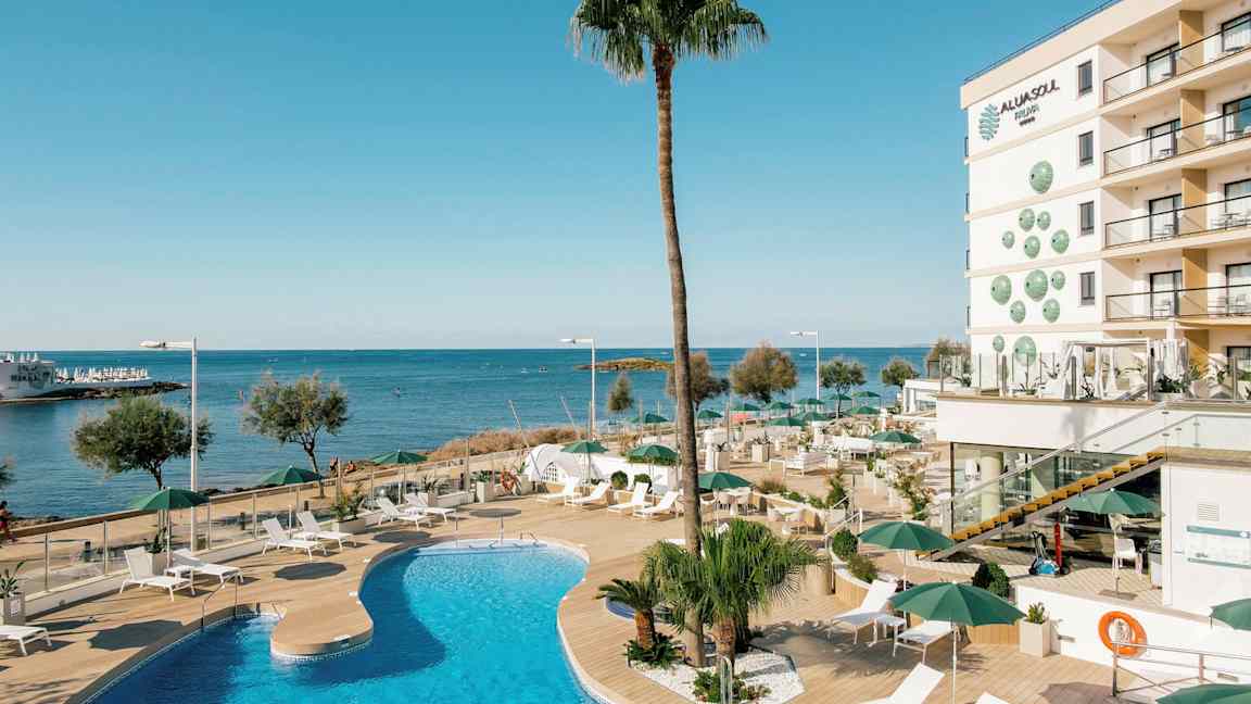 Et utendørs basseng ved et hotell nær havet med solsenger og parasoller på en treterrasse. (AI-generert tekst)