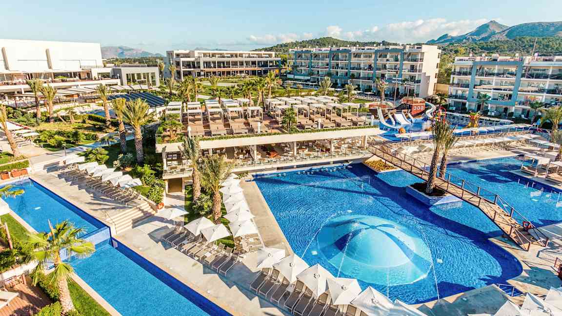 En utsikt over et hotellområde med bassenger, solsenger og bygninger. (AI-generert tekst)