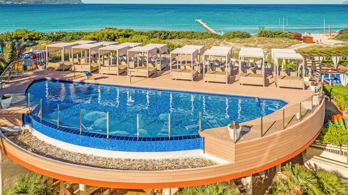 Utendørsbasseng med solsenger på en treterrasse nær stranden. (AI-generert tekst)