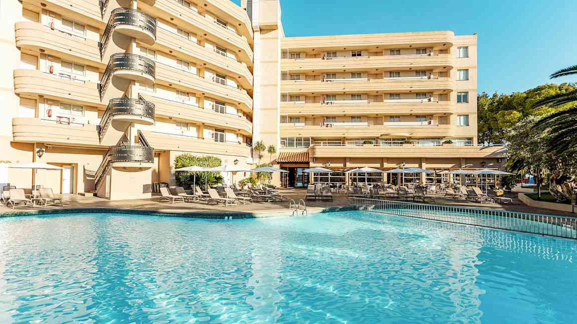 Hotellbygning ved et basseng med solsenger og parasoller. (AI-generert tekst)