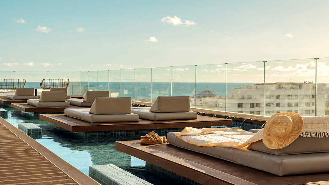 Liggeplasser ved et basseng med utsikt over byen og havet. (AI-generert tekst)