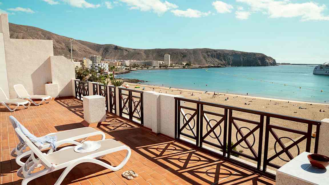 Terrasse med solsenger og utsikt over en sandstrand med havet i horisonten. (AI-generert tekst)