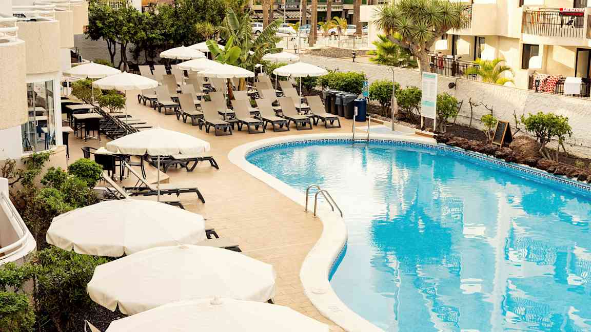 Bassengområde med solsenger og parasoller ved et hotell. (AI-generert tekst)