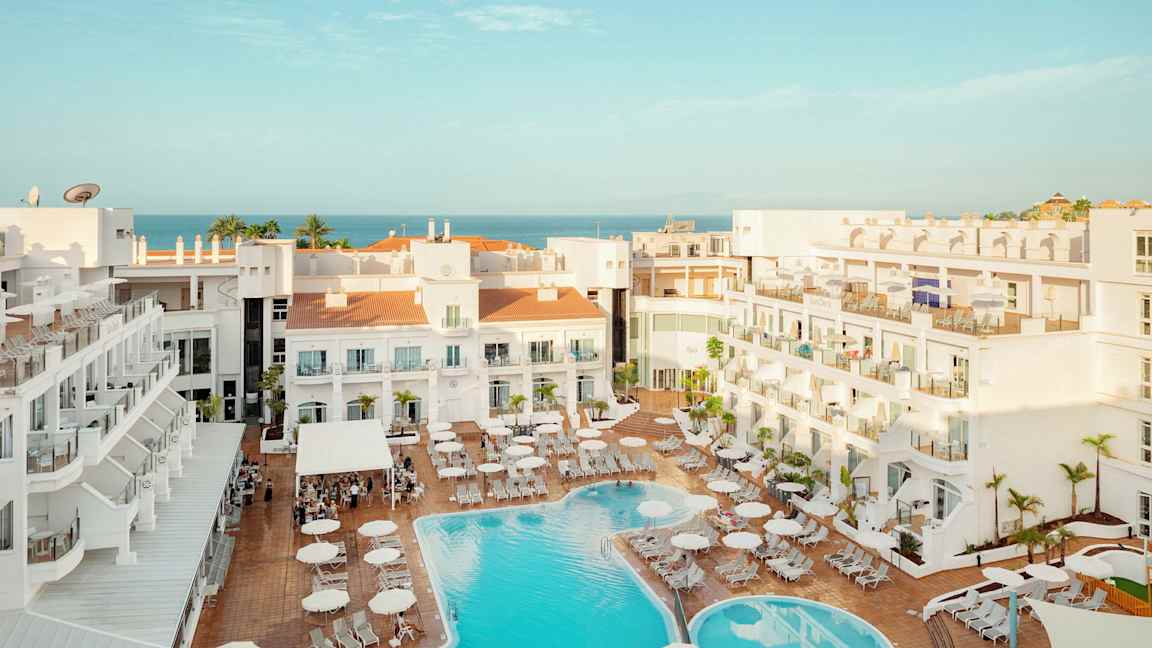 Utsikt over hotellområde med basseng og solsenger, havet er synlig i bakgrunnen. (AI-generert tekst)