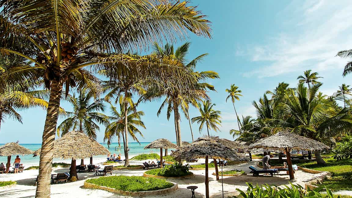 Strand med kokospalmer, parasoller og solsenger under en blå himmel. (AI-generert tekst)