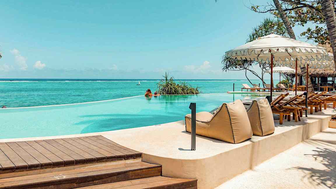 Et evighetsbasseng ved havet, omgitt av solsenger og parasoller. (AI-generert tekst)