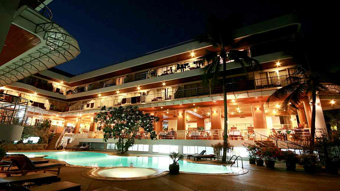 Kveldsvy av en fleretasjes bygning med opplyst fasade og et basseng i forgrunnen. (AI-generert tekst)