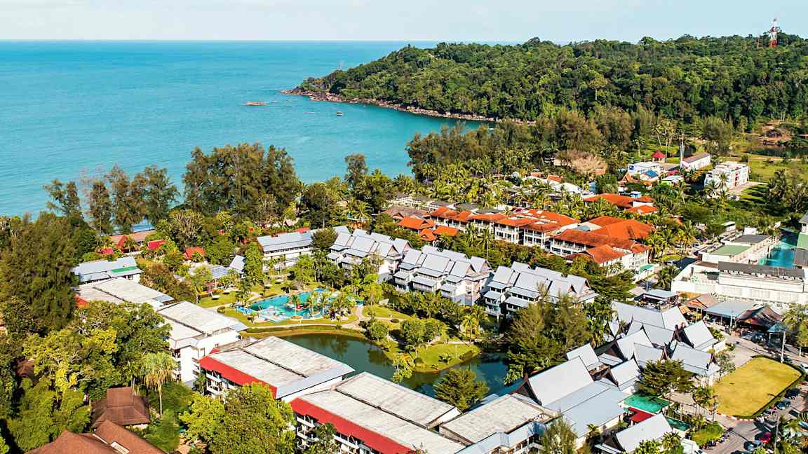 Luftfoto av et hotellkompleks omgitt av grønne områder ved sjøen. (AI-generert tekst)