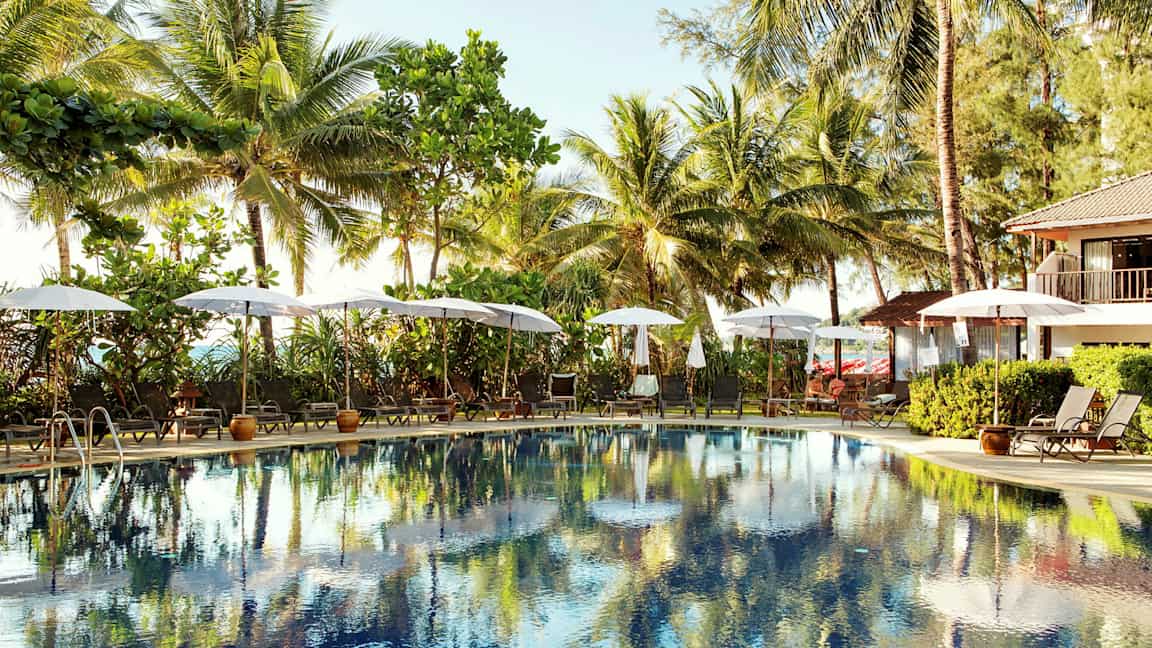 Utendørsbasseng omgitt av solsenger og parasoller, med palmer i bakgrunnen. (AI-generert tekst)