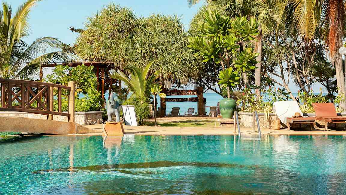 Et basseng med solsenger ved siden av, og bak er det trær og et skilt med teksten 'Lanta Villa'. (AI-generert tekst)