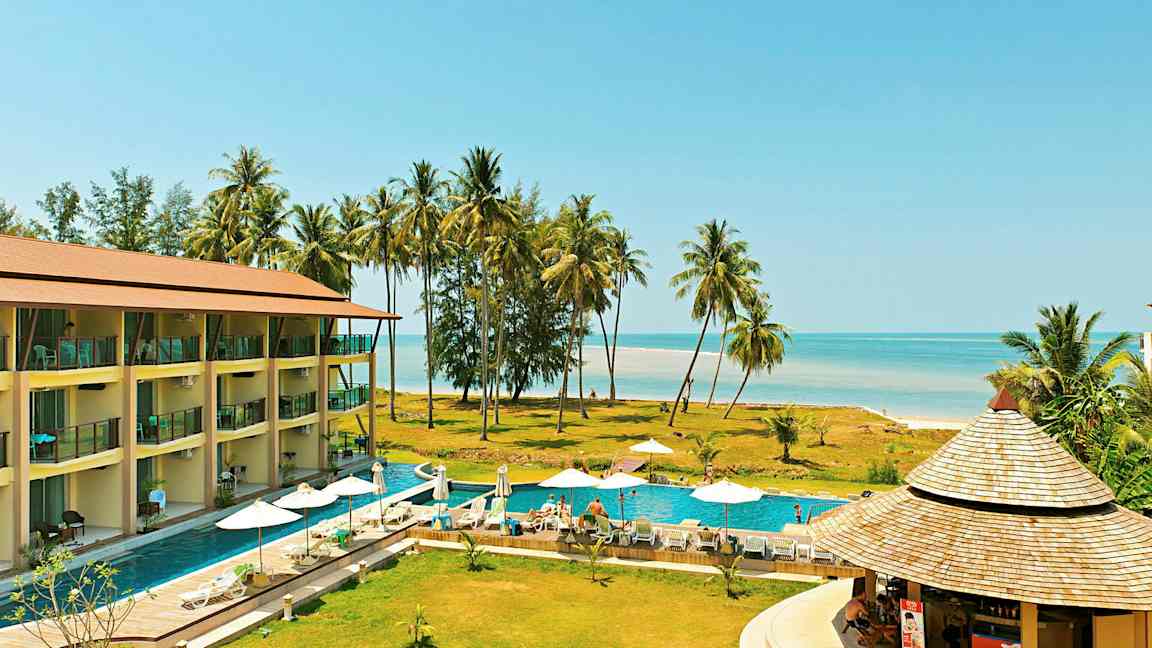 Et feriested med et basseng, solsenger og parasoller, nær stranden med palmer. (AI-generert tekst)