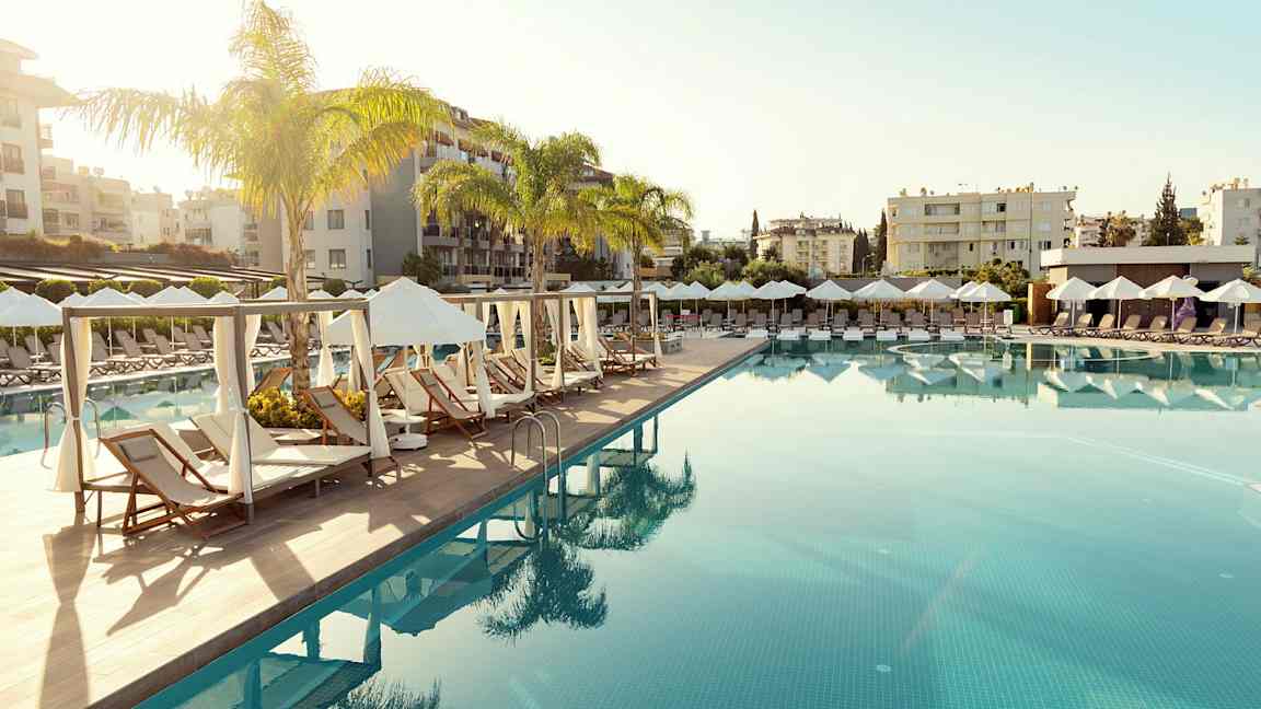 Et svømmebasseng med solsenger og parasoller i en feriestedmiljø. (AI-generert tekst)