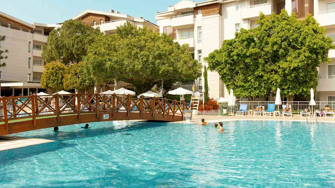 Utendørsbasseng med solsenger og trær i bakgrunnen. (AI-generert tekst)