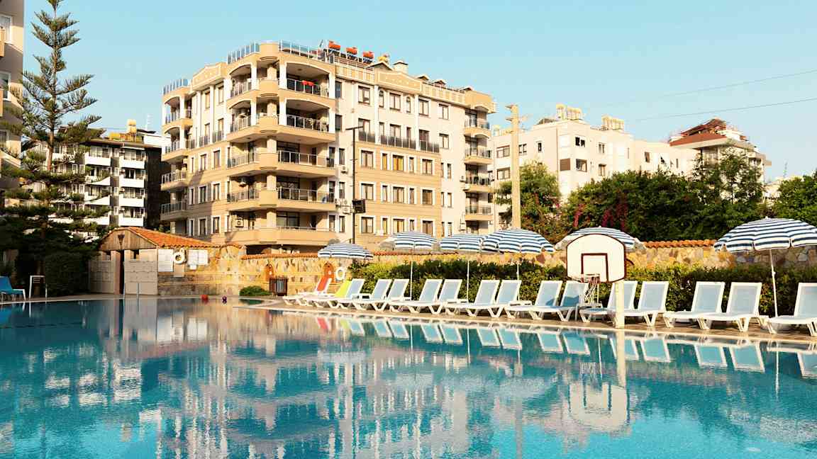 Bilde av et basseng med solsenger og parasoller på siden, samt en bygning i bakgrunnen. (AI-generert tekst)