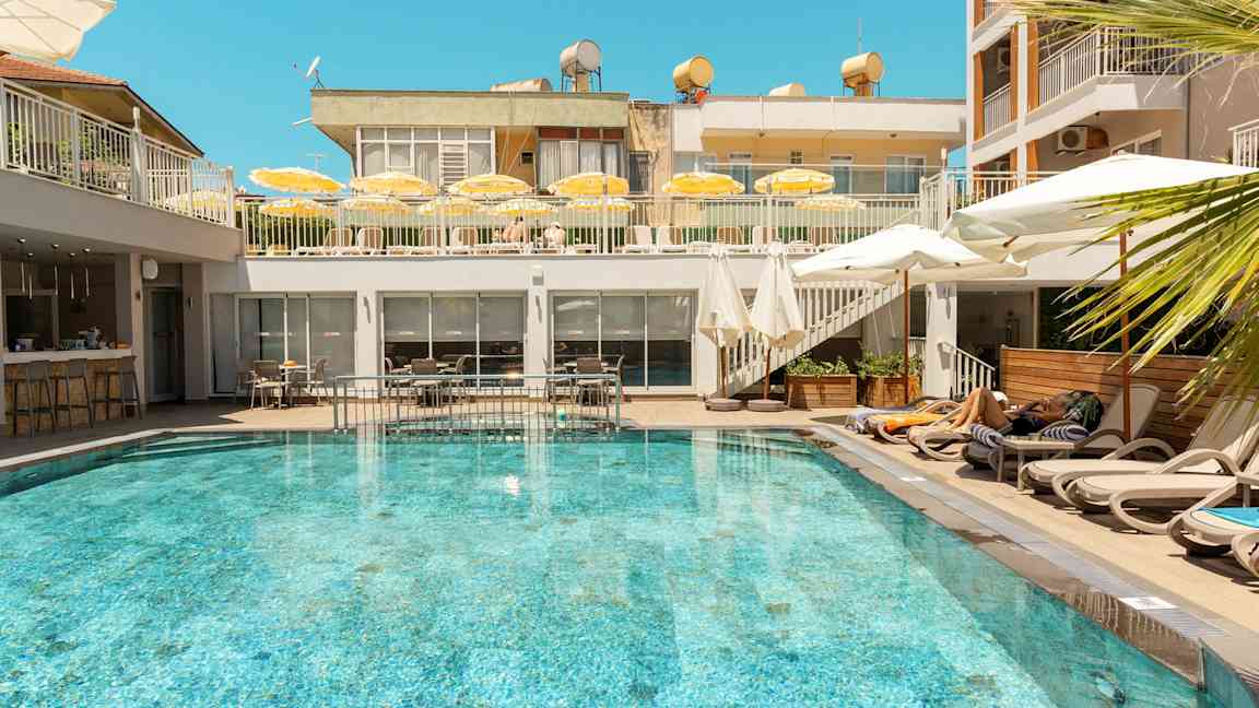Et utendørsbasseng omgitt av solsenger og parasoller på et hotell. (AI-generert tekst)