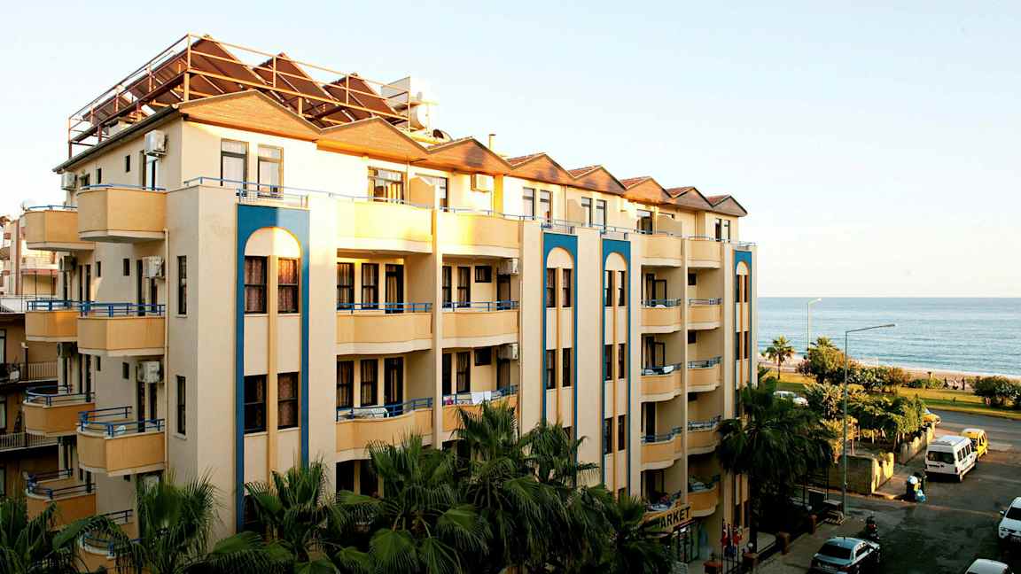 Bilde av en fleretasjes bygning med balkonger nær havet. (AI-generert tekst)