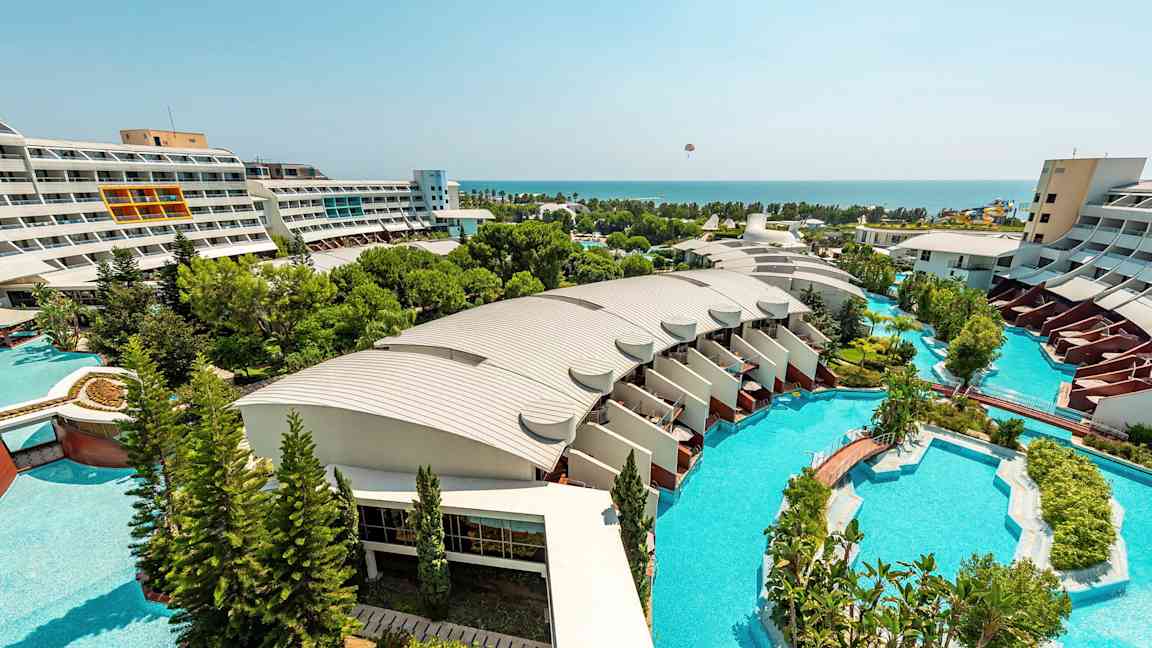 Utsikt over et hotellområde med moderne bygninger, store bassenger og frodige hager som strekker seg mot havet. (AI-generert tekst)