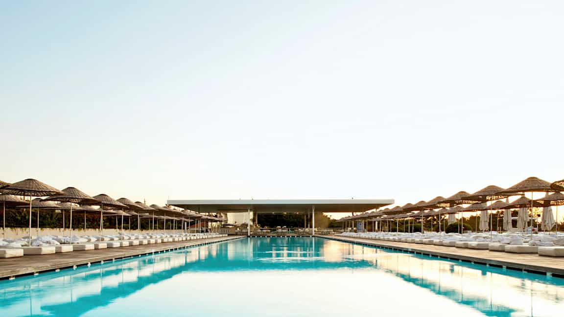 Et stort og langt basseng med parasoller og solsenger på begge sider. (AI-generert tekst)