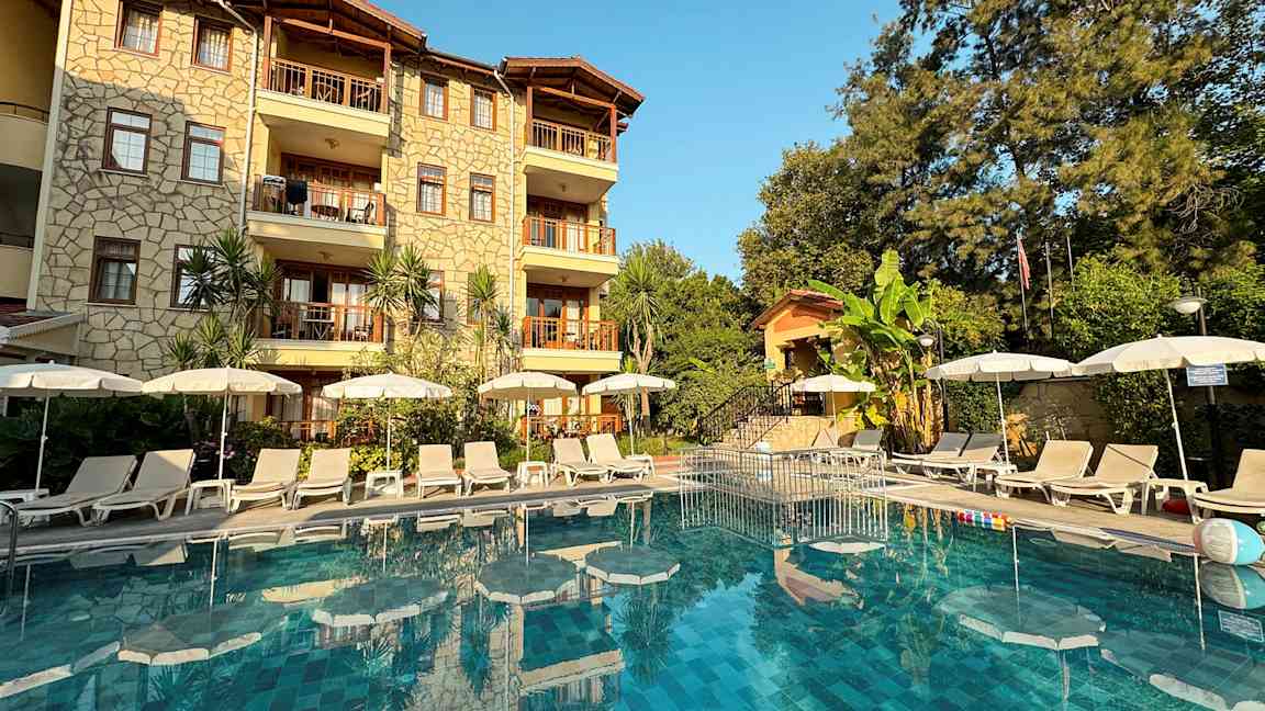 Bilde av hotellfasade med basseng og solsenger foran. (AI-generert tekst)