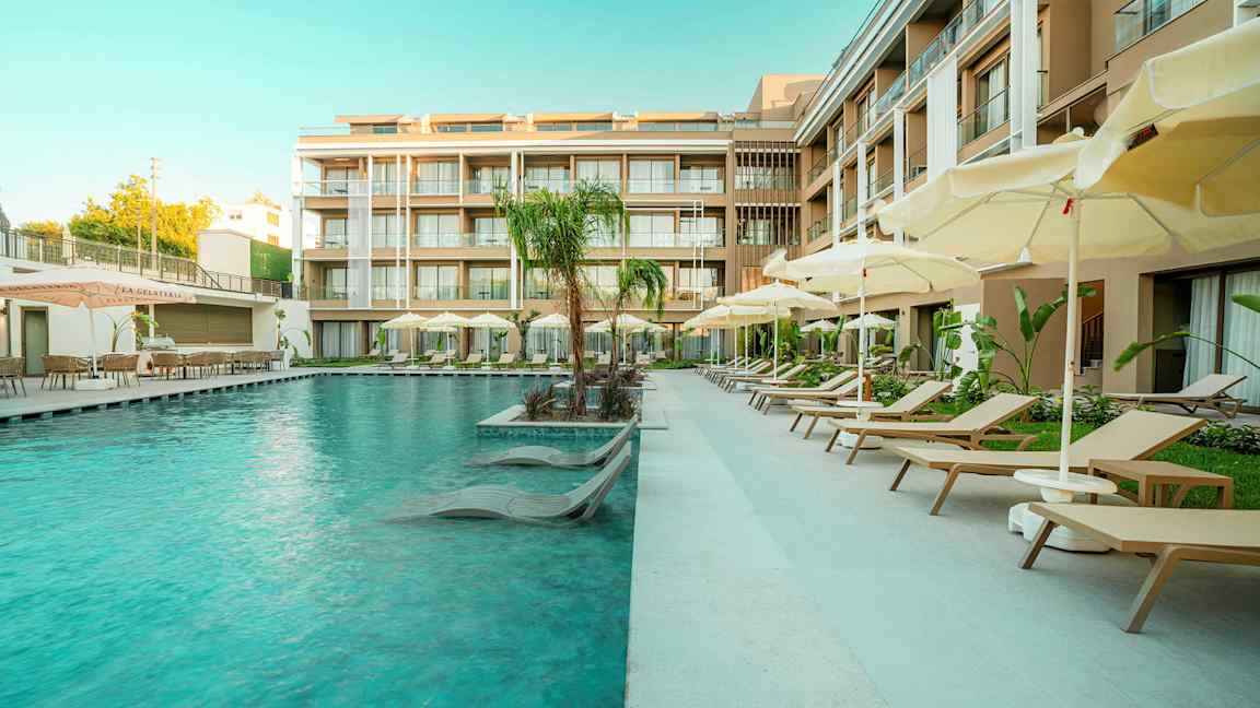 Et hotellbasseng med solsenger og parasoller ved siden av moderne bygninger. (AI-generert tekst)