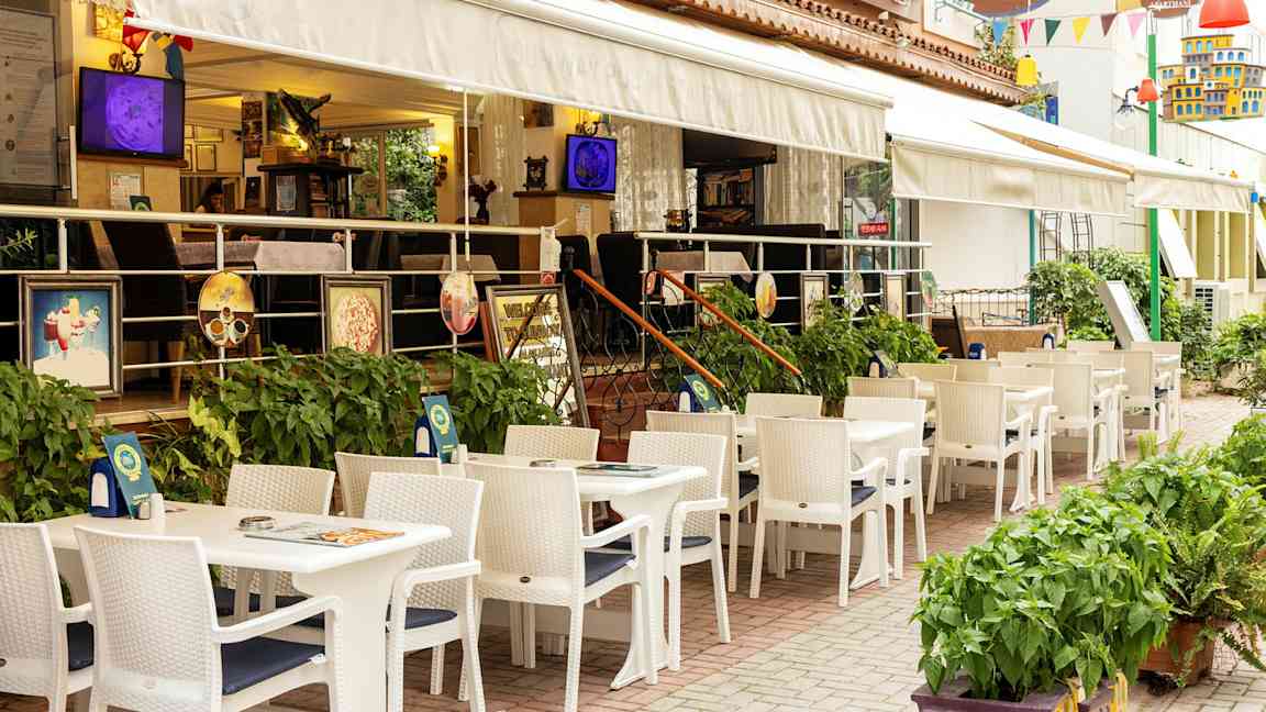Restaurant med uteservering med hvite bord og stoler ved et hotell. (AI-generert tekst)