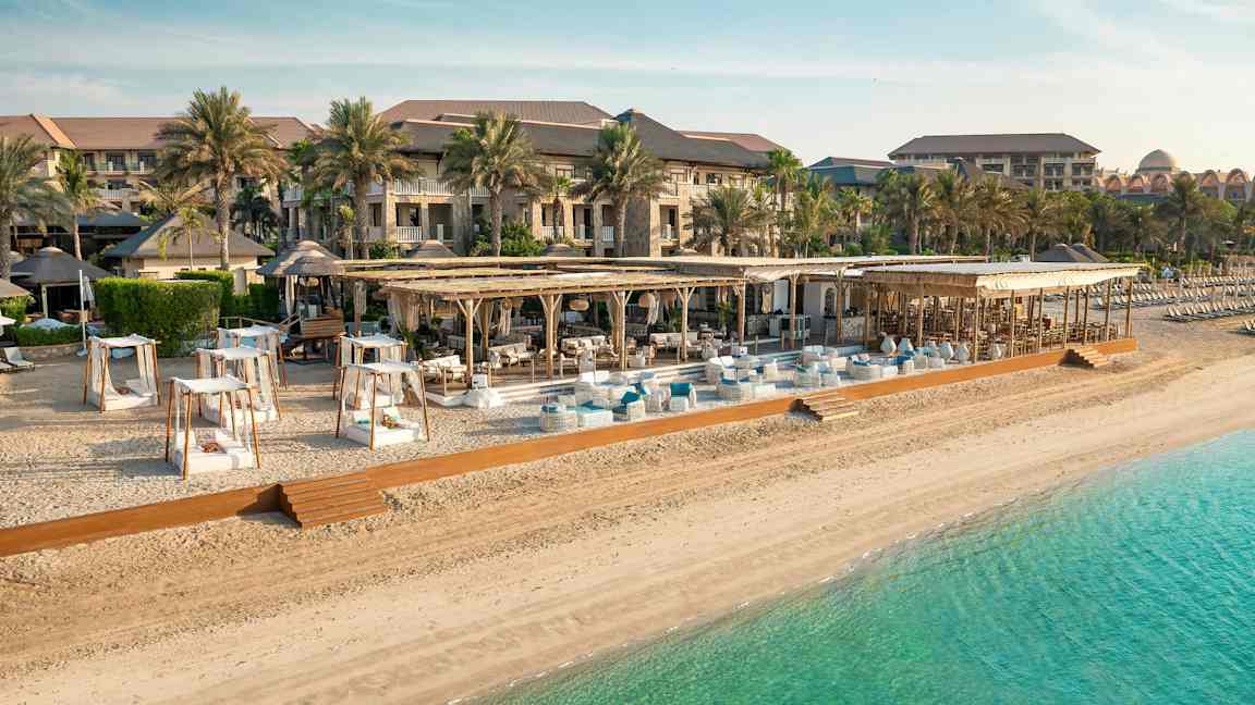 Strand med solsenger, parasoller og et hotell i bakgrunnen. (AI-generert tekst)