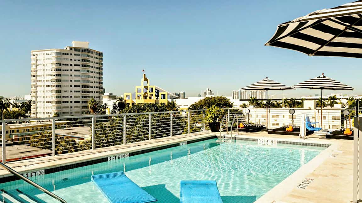 Et takbasseng omgitt av stripete parasoller, med utsikt over byen og flere bygninger i bakgrunnen. (AI-generert tekst)