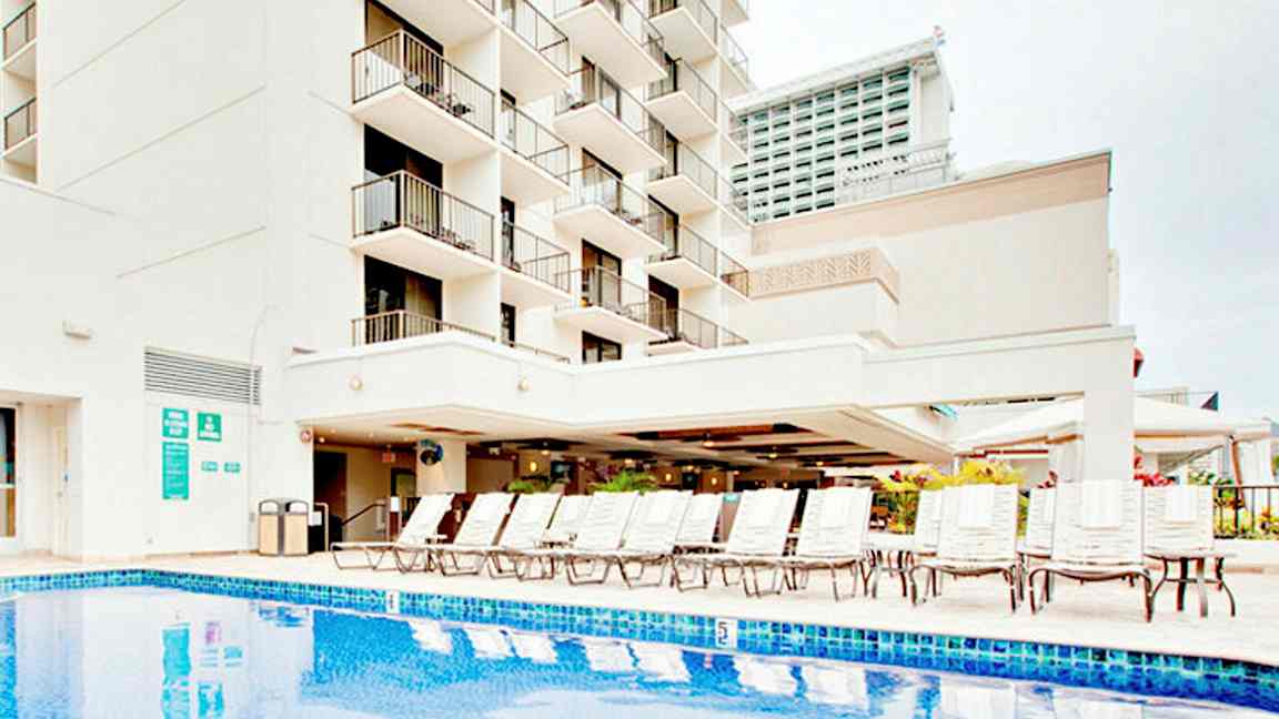 Bilde av en bygning med balkonger, et basseng og solsenger. (AI-generert tekst)